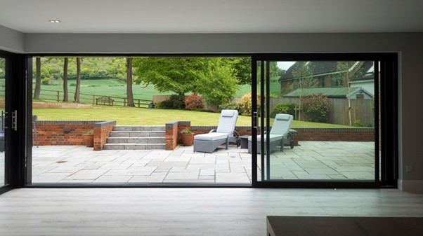 Half open sliding doors with the view of a garden with 2 deck chairs on a paved patio