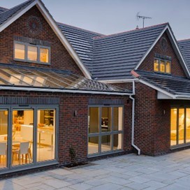 An evening view from the garden through corner doors into a bright kitchen and dining area
