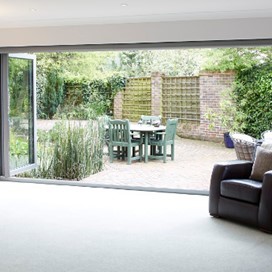 The view from a lounge looking through open bifolding doors, which cover a whole wall, into the garden
