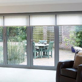 A full wall of floor to ceiling glass doors, each with a blind partially closed, looking into the garden