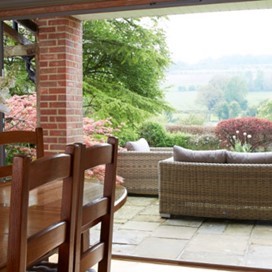 Looking over a dining table, through open patio doors and out into a paved area with wicker sofas