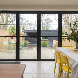 A set of closed bifold doors overlooking a modern homes garden with the view of a garden home in the background