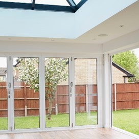 A garden room with wooden floors, a large skylight and large floor to ceiling glass doors across two walls