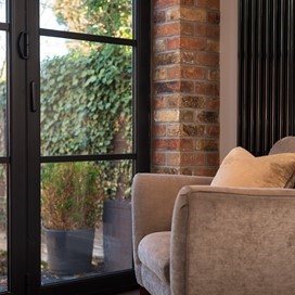 Cream chair in the corner of the room looking out through bifold doors to a garden