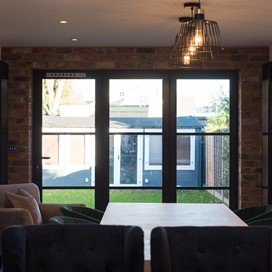 Large dining table surrounded by chairs next to closed bifold doors looking out towards the garden