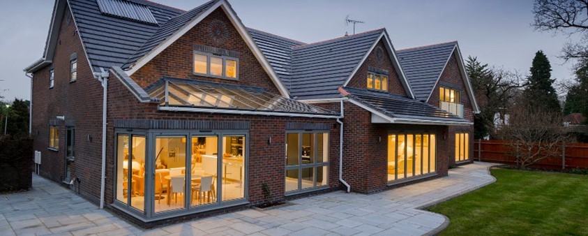 An evening view from the garden through corner doors into a bright kitchen and dining area