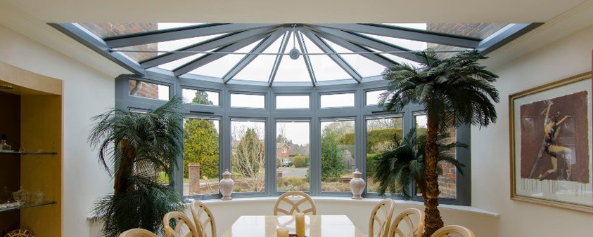 An internal view of a bay windowed dining room with a glass ceiling overhead