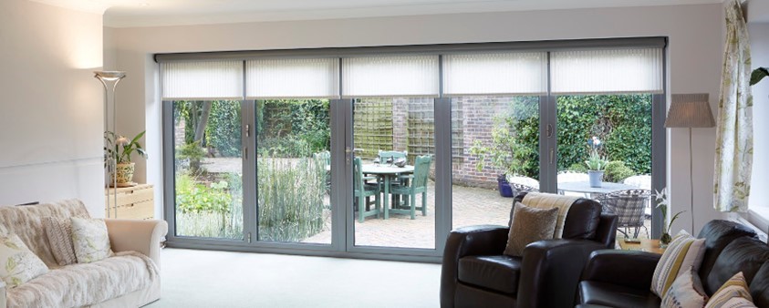 A full wall of floor to ceiling glass doors, each with a blind partially closed, looking into the garden