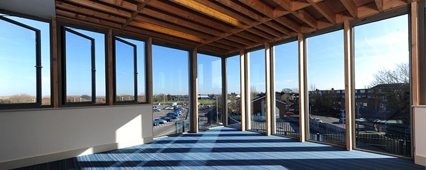 Looking into the corner of the room and out through large windows over a car park