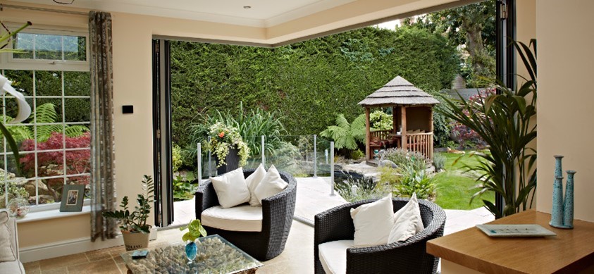 Looking out through open folding doors into a garden with a lawn and gazebo