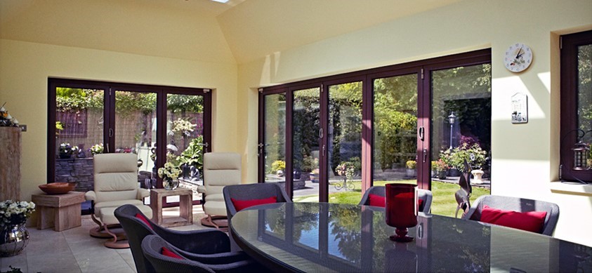 A bright house extension with a large table, comfortable chairs and large folding doors out to the garden
