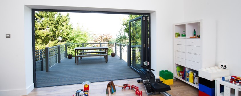 A bright room looking out through fully opened folding doors onto an upper storey decking area