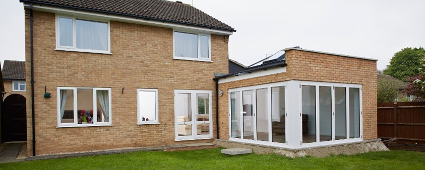 A view from the lawn at the back of a house with an extension featuring a large corner door