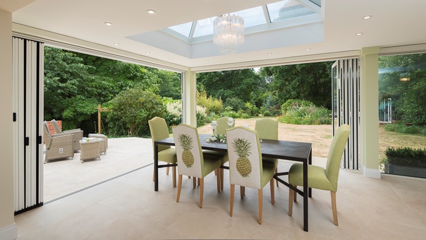 Set of green chairs around a dining table facing the garden through a open white bifold door
