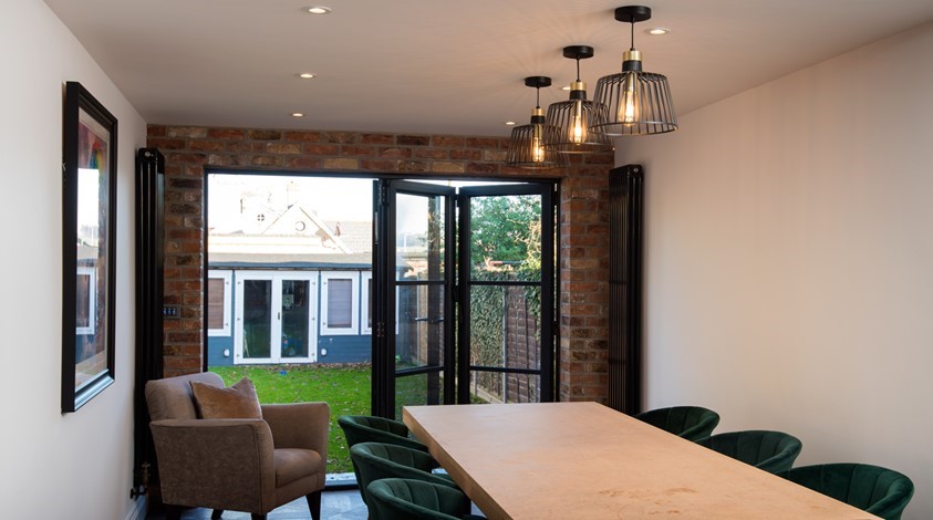 Large dining table surrounded by chairs next to half open bifold doors looking out towards the garden