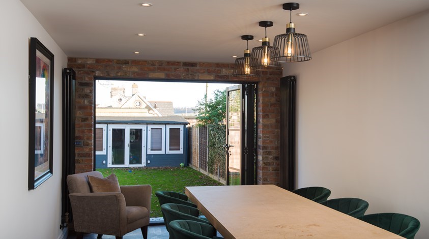 Large dining table surrounded by chairs next to open bifold doors looking out towards the garden