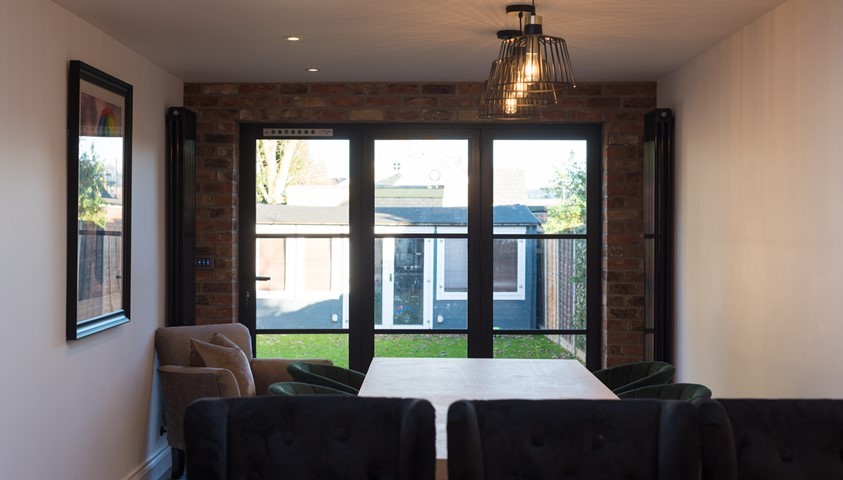 Large dining table surrounded by chairs next to closed bifold doors looking out towards the garden