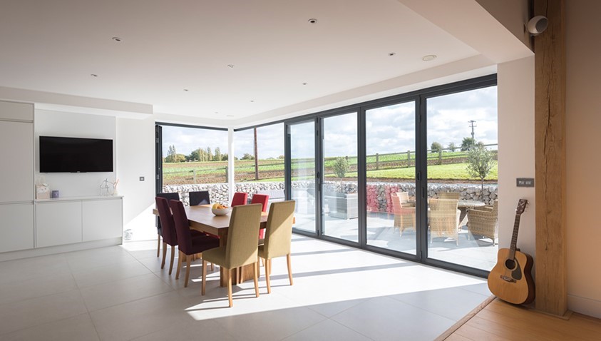 Indoor dining set of table and chairs overlooking garden through set of bifold doors 