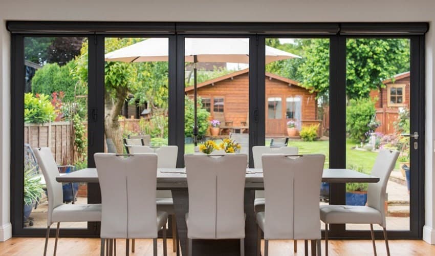 Grey aluminium bifold doors looking over a garden with a dining table in front