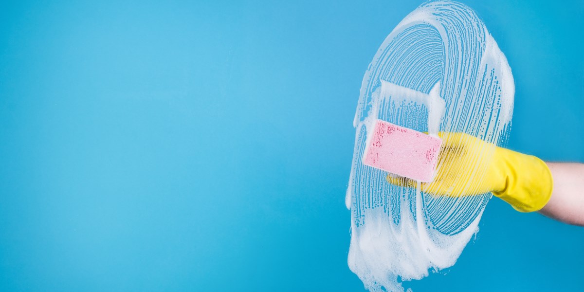 A person cleaning a window with a sponge and multipurpose cleaner.