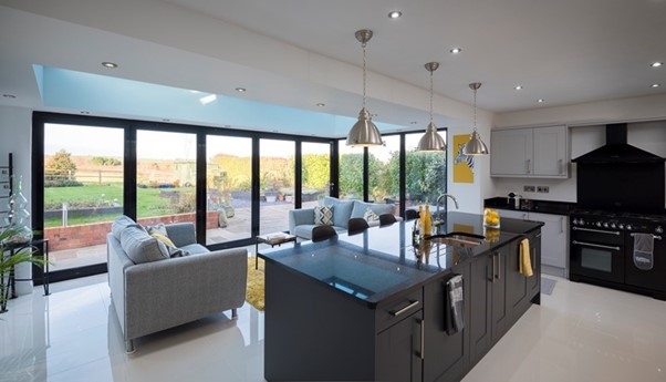 A well-lit open-plan island kitchen and social area with corner bifold doors. 